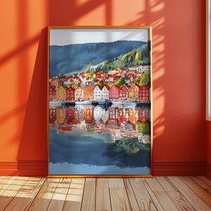 May include: A framed watercolor painting of a colorful waterfront town with buildings in shades of red, orange, yellow, and white. The buildings are reflected in the water below, with a mountain in the background.