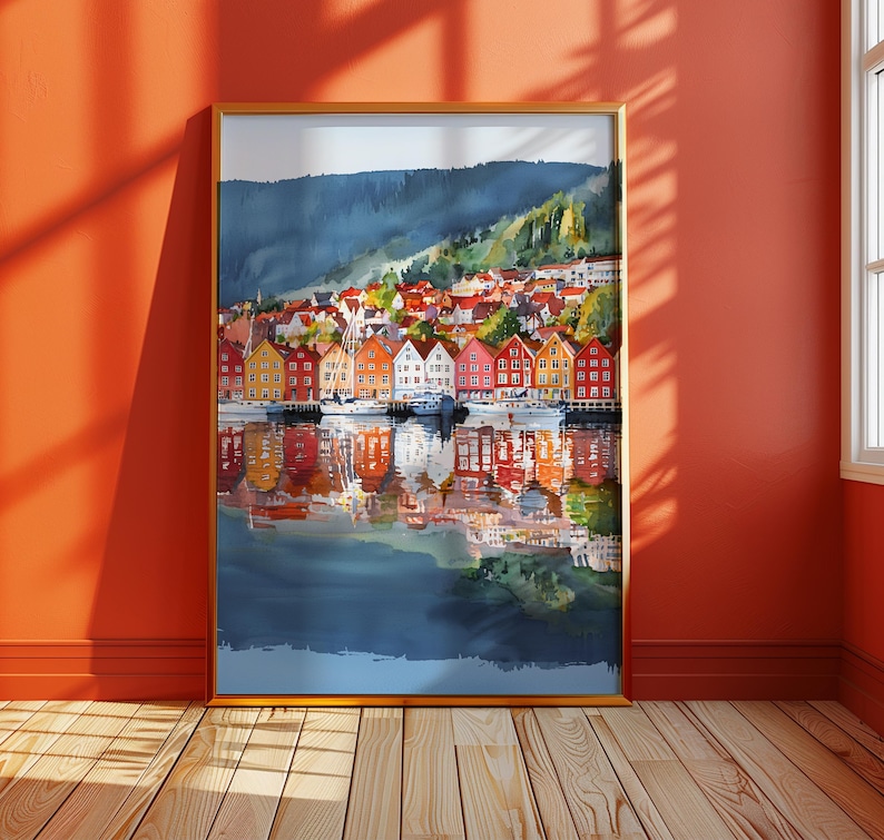 May include: A framed watercolor painting of a colorful waterfront town with buildings in shades of red, orange, yellow, and white. The buildings are reflected in the water below, with a mountain in the background.