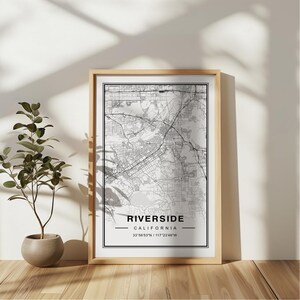 May include: A black and white map print of Riverside, California. The map shows the city streets and landmarks. The text below the map reads "Riverside, California 33.9583°N | 117.2346°W".
