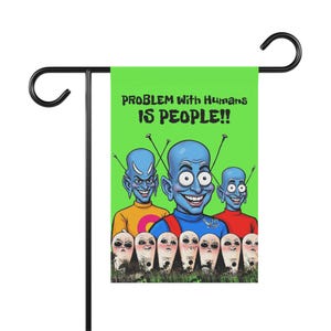 May include: A green garden flag with the text "PROBLEM WITH HUMANS IS PEOPLE!!" features a cartoon image of blue-skinned aliens with antennas and smiling faces. Below them are white, egg-shaped creatures with various expressions.