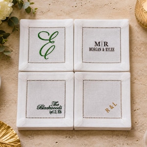 May include: Four white square coasters with embroidered details. Each coaster features a different design: a green letter "E", "MR MORGAN & RYLEE", "The Blackwoods April 23, 2026", and gold letters "R&L".