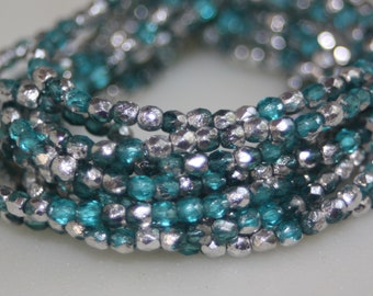 Op de afbeelding: Een close-up van een meerstrengige armband gemaakt met teal en zilveren kralen. De kralen zijn facetgeslepen en hebben een metallic glans.