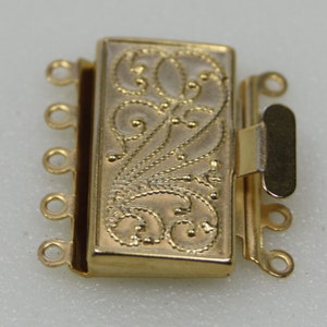 Puede incluir: Un cierre de joyería dorado para múltiples hilos. El cierre rectangular presenta un diseño floral grabado y ornamentado. Tiene cuatro bucles en un lado y un cierre en el otro. El componente de joyería está diseñado para conectar múltiples hilos.