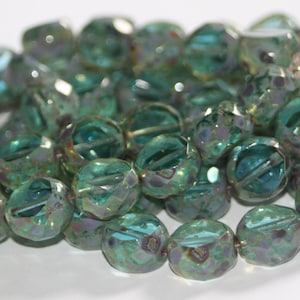 May include: A collection of iridescent teal glass beads. The beads have a faceted, round shape with a hole for stringing. The beads have a mix of teal, purple, and gold colors. The beads are suitable for jewelry making and crafts.