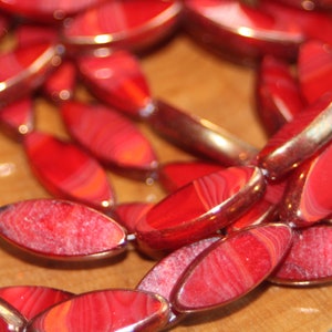 May include: A strand of red and orange agate beads with a glossy finish. The beads are oval shaped and have a natural, striated pattern.