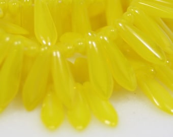 May include: A close-up of a bunch of bright yellow glass beads shaped like teardrops. The beads are arranged in a random pattern, creating a visually appealing texture.