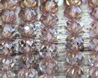 May include: Close-up of strands of faceted, light pink beads. The beads have a clear, crystal-like appearance with gold-colored accents. The beads are round with a cut-glass design, and are strung together.