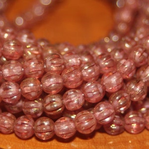 May include: A strand of pink glass beads with a metallic sheen. The beads are round and have a textured surface.