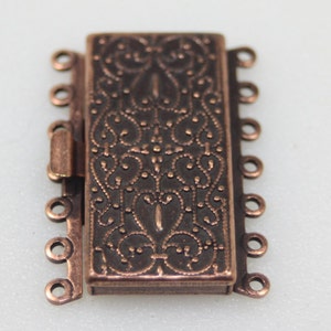 May include: A copper-toned metal clasp with a decorative design and five loops for attaching jewelry.