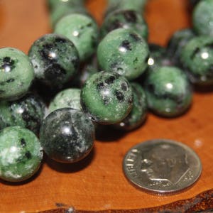 May include: A strand of green and black gemstone beads. The beads are round and have a speckled pattern.