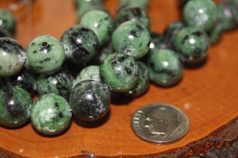 May include: A strand of green and black gemstone beads. The beads are round and have a speckled pattern.