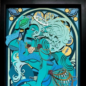 May include: A papercraft artwork depicting a mermaid with a crown of seaweed, holding a seashell. The mermaid is blue and green with a gold net and a pink flower on her shoulder. The background is a blue and green stained glass design.