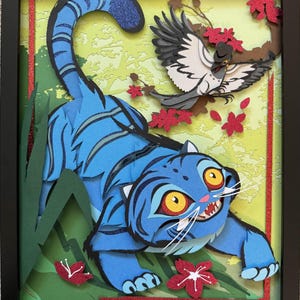 May include: A framed paper art piece featuring a blue tiger with black stripes, yellow eyes, and a snarling expression. A gray bird with a hat perches on a branch with red flowers. The background is a light green with red accents.