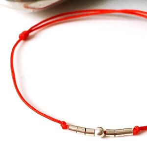 May include: A red string bracelet with silver beads, including a larger round bead in the center.