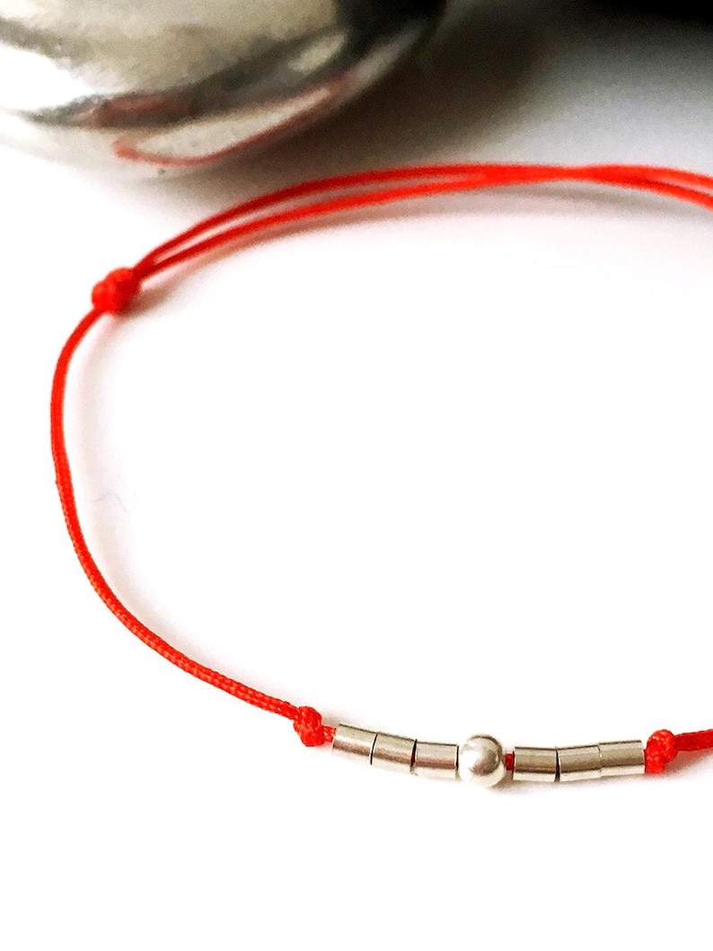 May include: A red string bracelet with silver beads, including a larger round bead in the center.