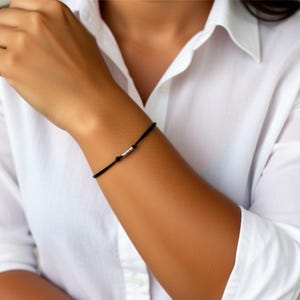 Bracciale in cordino nero con 3 perline tubolari in argento sterling e 1 perlina tubolare in argento sterling sul retro del bracciale. Elegante gioiello protettivo parigino.