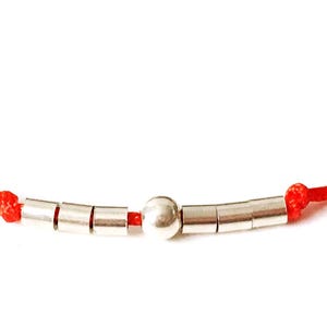 May include: A red string bracelet with silver beads, including a larger round bead in the center.