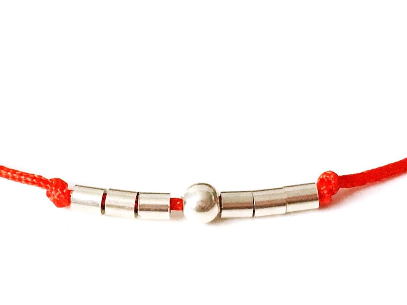 May include: A red string bracelet with silver beads, including a larger round bead in the center.