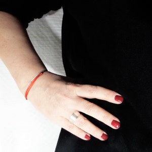 Puede incluir: Una pulsera de hilo rojo y una pulsera de plata se llevan en la mu&ntilde;eca de una persona. La persona lleva una camiseta negra y tiene esmalte de u&ntilde;as rojo en las u&ntilde;as. Un anillo de plata est&aacute; en el dedo de la persona.