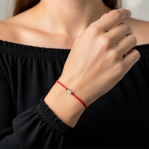 Pulsera de cordón rojo con un tubo redondeado de plata de ley, que presenta una letra T en código Morse y una cuenta tubular de plata de ley en la parte posterior. Joyería protectora.