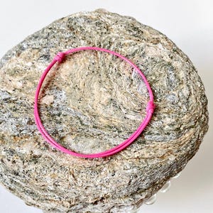 May include: A pink cord bracelet on a textured rock background.