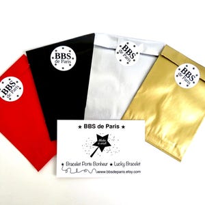 Puede incluir: Una variedad de bolsas de regalo coloridas en rojo, negro, blanco y dorado, cada una sellada con una pegatina que dice "BBS de Paris". Tambi&eacute;n hay una tarjeta de visita con el texto "BBS de Paris" y "Make a wish".