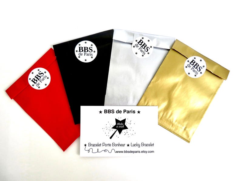 Puede incluir: Una variedad de bolsas de regalo coloridas en rojo, negro, blanco y dorado, cada una sellada con una pegatina que dice "BBS de Paris". Tambi&eacute;n hay una tarjeta de visita con el texto "BBS de Paris" y "Make a wish".