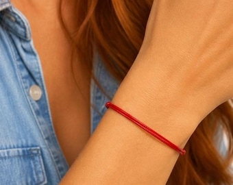 Könnte beinhalten: Ein einfaches, dünnes rotes Schnurarmband am Handgelenk. Das Armband besteht aus einem einzelnen, glatten, leuchtend roten Faden, der das Handgelenk umschließt, und zeichnet sich durch ein minimalistisches Design ohne sichtbare Anhänger oder Metallteile aus.