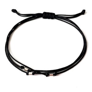 May include: Black adjustable bracelet featuring three cords and small silver-colored cylindrical beads. The bracelet is knotted at the top for adjustment and is set against a white background. A simple, minimalist design.