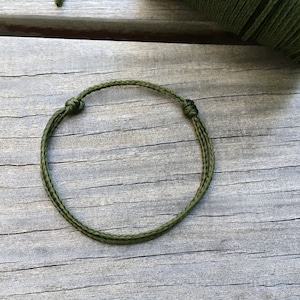 Peut inclure: Un bracelet en paracorde vert avec deux nœuds sur une surface en bois.