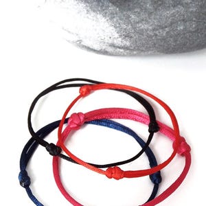 Puede incluir: Cuatro pulseras ajustables en rojo, negro, azul y rosa. Cada pulsera presenta un dise&ntilde;o anudado y est&aacute; hecha de un cord&oacute;n fino y flexible. Las pulseras se muestran sobre una superficie blanca.