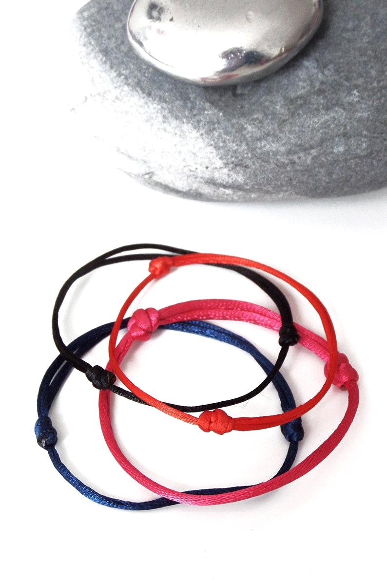 Puede incluir: Cuatro pulseras ajustables en rojo, negro, azul y rosa. Cada pulsera presenta un dise&ntilde;o anudado y est&aacute; hecha de un cord&oacute;n fino y flexible. Las pulseras se muestran sobre una superficie blanca.