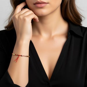 Rotes Kordelarmband mit einer 14-karätigen Goldperle und winzigen dreieckigen goldenen Hämatitperlen. Kostbarer Schmuck aus Gold und Hämatitperlen.