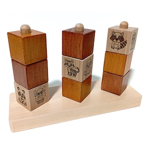 Peut inclure: Un jouet d'empilage en bois avec trois tours de blocs. Chaque tour a quatre blocs avec des motifs d'animaux différents. Les blocs sont empilés sur une base en bois.