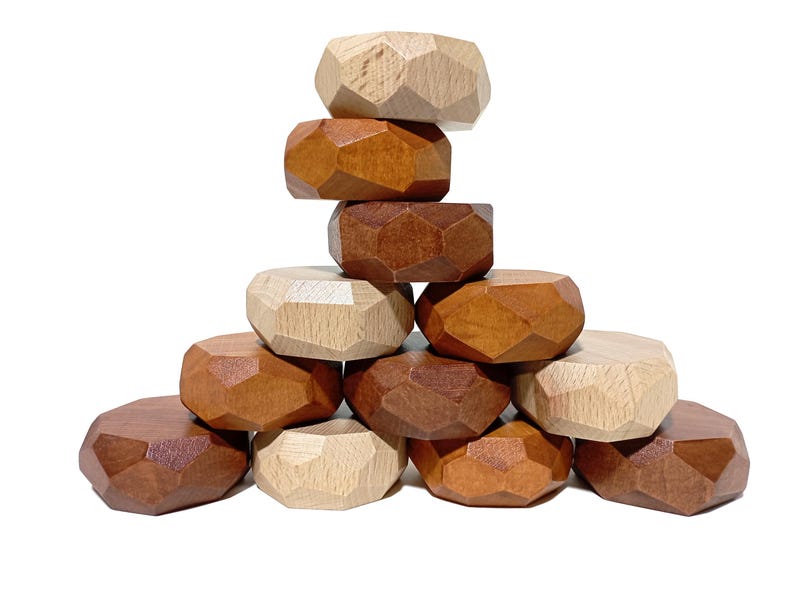 May include: A stack of 10 wooden geometric shapes in brown, light brown, and natural wood tones. The shapes are stacked in a pyramid formation.