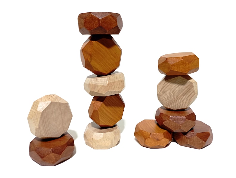 May include: A stack of wooden geometric blocks in brown and natural wood tones. The blocks are stacked in a tower with a few blocks on the bottom forming a base.