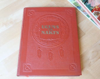 May include: A red hardcover book with a gold embossed design and the title "Uguns Nakts" on the front cover.