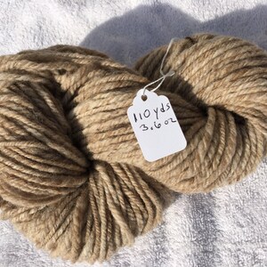 May include: A skein of beige yarn with brown flecks. The yarn is tied with a white tag that reads "110 yds 3.16 oz".