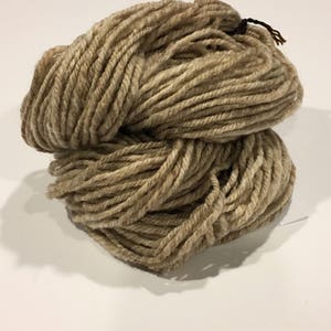 May include: A skein of beige yarn, made of natural fibers, is shown in a close-up view. The yarn is soft and fluffy, and it is perfect for knitting or crocheting.