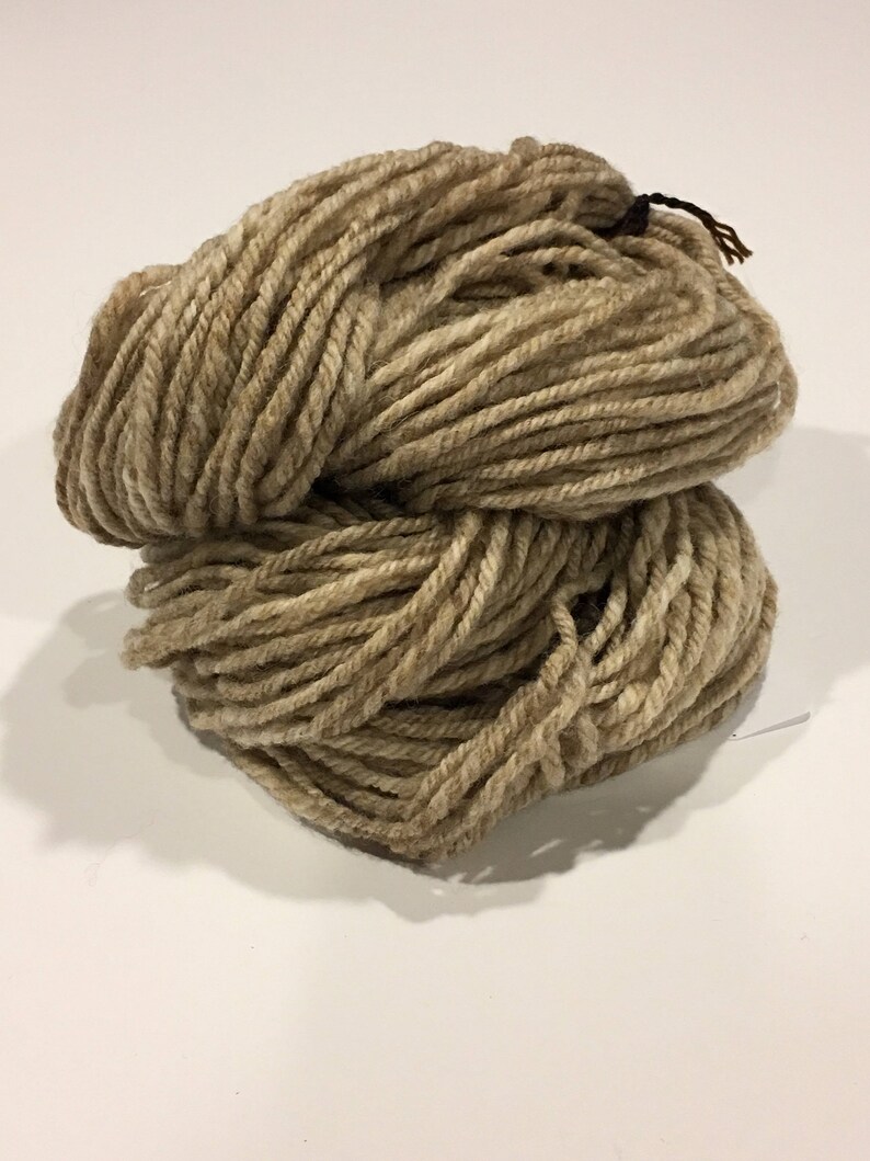 May include: A skein of beige yarn, made of natural fibers, is shown in a close-up view. The yarn is soft and fluffy, and it is perfect for knitting or crocheting.