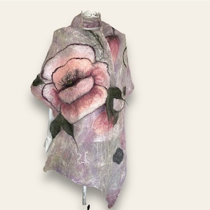 Op de afbeelding: Een lichtpaarse en roze vilten wollen sjaal met een groot roze bloemenontwerp. De bloem heeft een donkerroze centrum en groene bladeren.