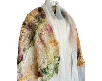 May include: A colorful, abstract wool scarf with a white sheer scarf draped over it. The wool scarf has shades of brown, orange, green, and pink.