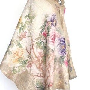 K&ouml;nnte beinhalten: Ein beiger Umhang mit einem Blumendesign mit rosa, lila und gelben Pfingstrosen, gr&uuml;nen Bl&auml;ttern und braunen Zweigen. Der Umhang hat einen Kragen und wird auf einem wei&szlig;en Kleiderb&uuml;gel pr&auml;sentiert.