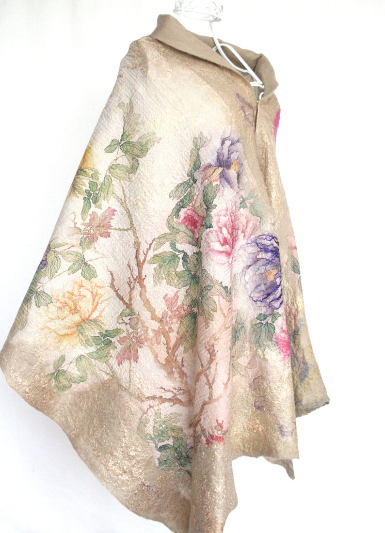 K&ouml;nnte beinhalten: Ein beiger Umhang mit einem Blumendesign mit rosa, lila und gelben Pfingstrosen, gr&uuml;nen Bl&auml;ttern und braunen Zweigen. Der Umhang hat einen Kragen und wird auf einem wei&szlig;en Kleiderb&uuml;gel pr&auml;sentiert.