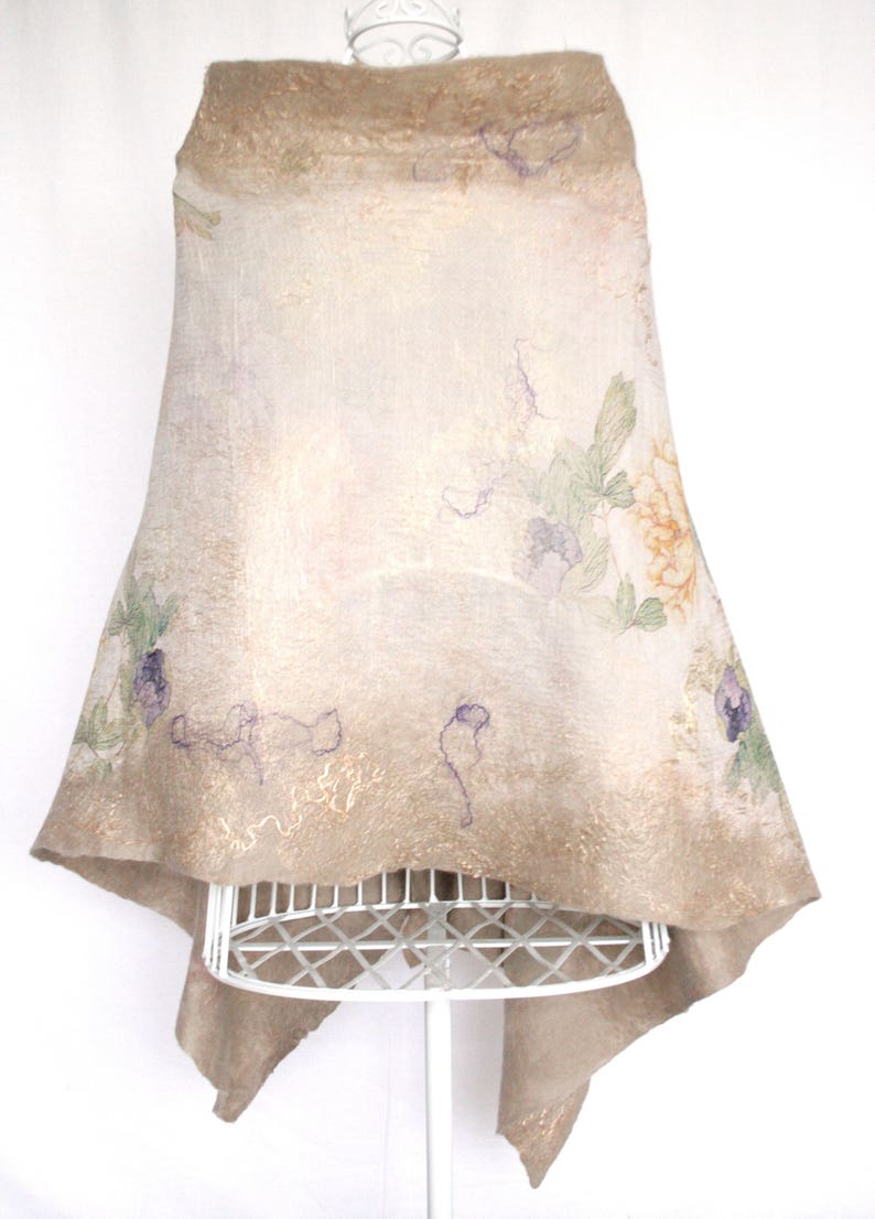 K&ouml;nnte beinhalten: Ein beigefarbener Filzschal mit floralen und abstrakten Designs. Der Schal wird auf einer wei&szlig;en Schaufensterpuppe pr&auml;sentiert. Das florale Design umfasst violette, gr&uuml;ne und orange Farbt&ouml;ne. Die Kanten des Schals haben einen Goldschimmer.