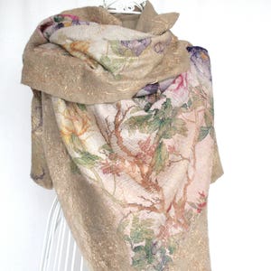 K&ouml;nnte beinhalten: Beigefarbener Schal mit einem Blumenmuster in Rosa, Lila, Gr&uuml;n und Gelb. Der Schal hat eine strukturierte Optik mit goldenen Akzenten und ist &uuml;ber einem wei&szlig;en Drahtgestell drapiert.