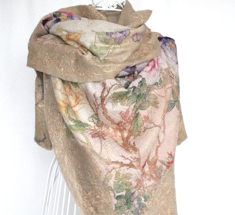 K&ouml;nnte beinhalten: Beigefarbener Schal mit einem Blumenmuster in Rosa, Lila, Gr&uuml;n und Gelb. Der Schal hat eine strukturierte Optik mit goldenen Akzenten und ist &uuml;ber einem wei&szlig;en Drahtgestell drapiert.