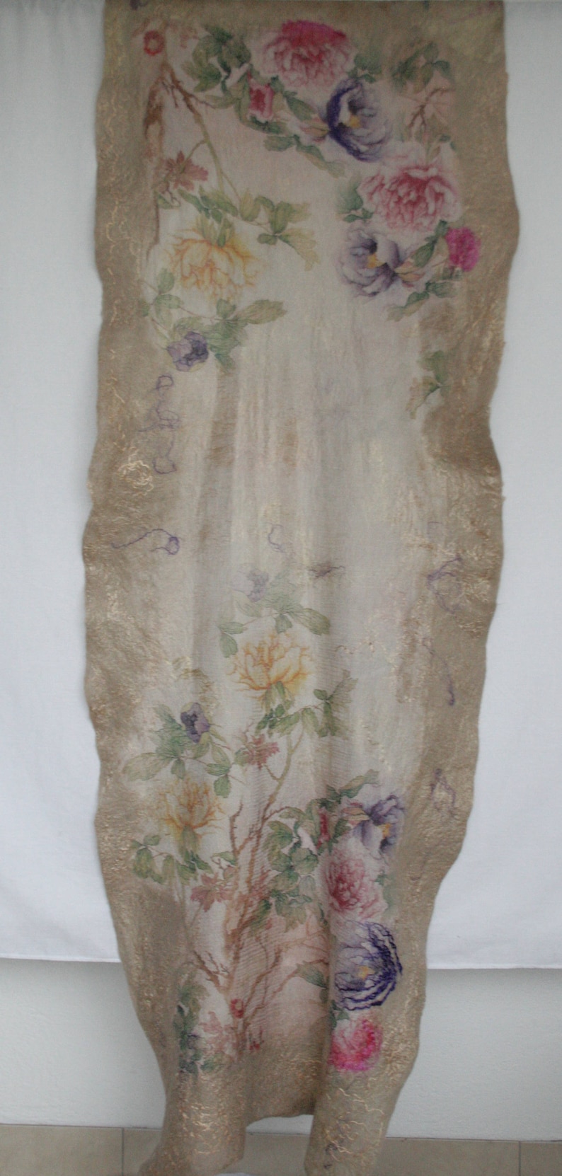 K&ouml;nnte beinhalten: Ein langes, rechteckiges Textil mit floralem Design. Der Stoff hat einen cremefarbenen Hintergrund mit rosa, lila und gelben Blumen und gr&uuml;nen Bl&auml;ttern. Die R&auml;nder sind mit einem goldenen Rand versehen.