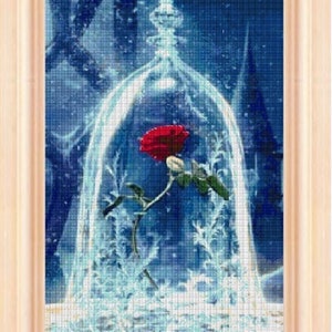 Può includere: Una singola rosa rossa è racchiusa in una cupola di vetro, circondata da uno sfondo blu e bianco innevato. La rosa è in fiore e ha foglie verdi. Il testo "Enchanted Rose - Neni Design" è in basso nell'immagine.