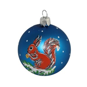 May include: A blue Christmas ornament with a painted image of a red squirrel holding a nut on a snowy branch.